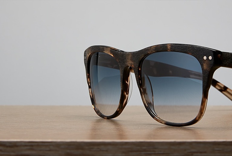 Premium square sunglasses #113435 with light gray tint on a wood table top.