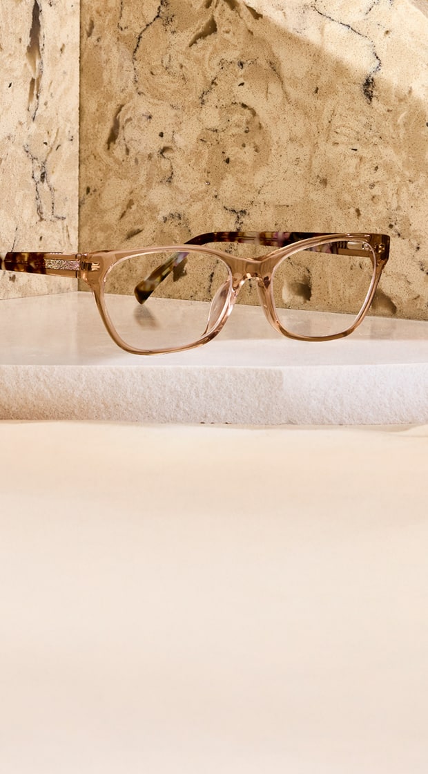 Light brown rectangle Zenni glasses with tortoiseshell temple arms on a polished beige stone background.