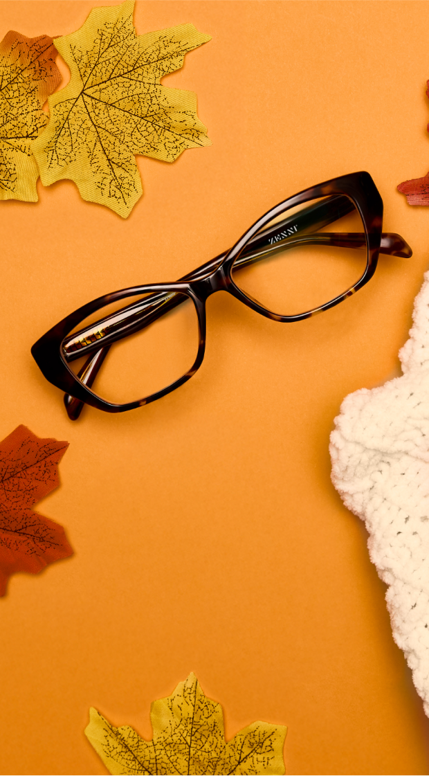 Cat-eye tortoiseshell frames on an orange surface next to fall leaves and a beige knit scarf.