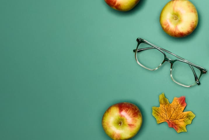 Green ombre square glasses on a green background with apples, fall leaves, and a plaid scarf.