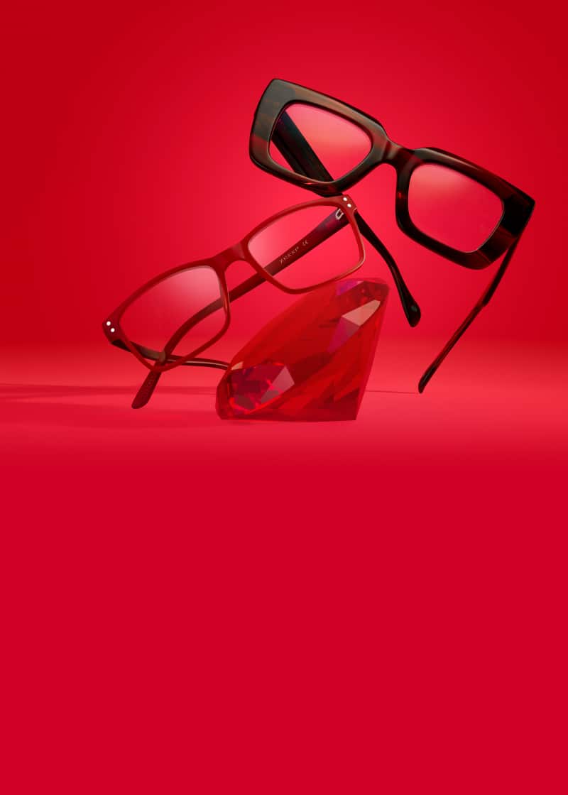 Oversized red rectangle glasses and rectangle red glasses resting on a giant red ruby, on a bright red background.