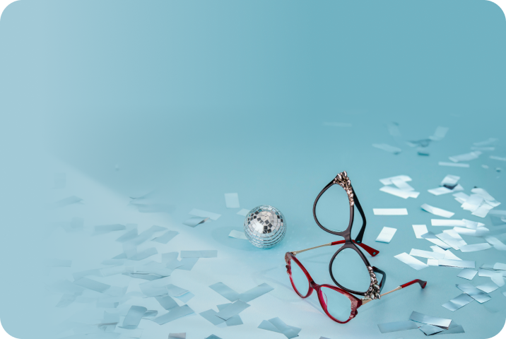 Image of two jeweled glasses and a disco ball on a light blue surface covered in silver confetti.