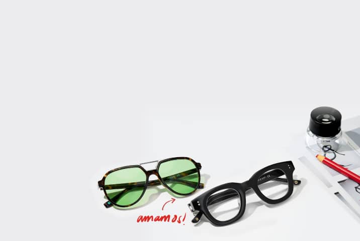 Gafas de aviador de carey con lentes verdes y un detalle de doble puente plateado, junto a unas gafas negras de montura gruesa y marcada, sobre una superficie blanca con la frase «¡me encantan!» escrita en rojo.