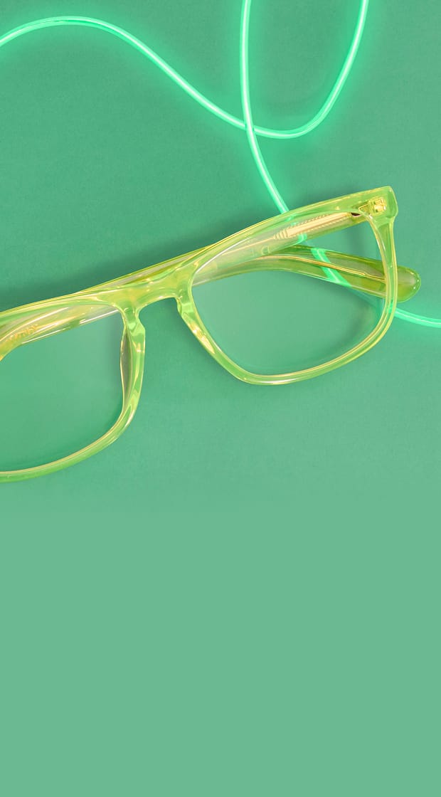 A pair of translucent neon yellow-green eyeglasses is placed on a matching green background, accented by a glowing, looping green neon light strand.