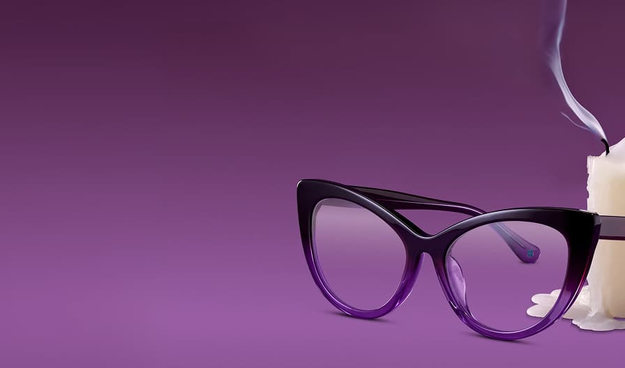 Dark purple gradient cat-eye eyeglasses resting next to a melting white pillar candle against a deep purple background.