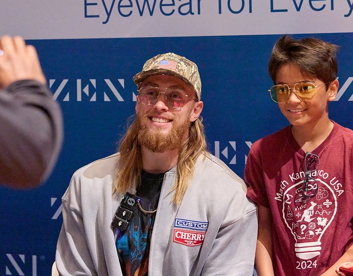George Kittle smiling with a child wearing Zenni glasses at a community event booth.