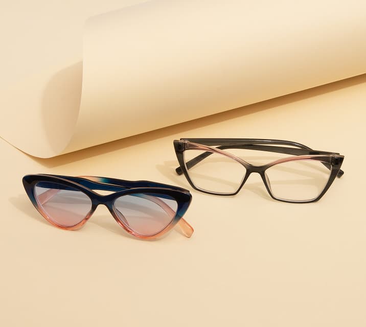Two pairs of stylish eyeglasses on a beige background. One pair features cat-eye frames in a gradient of blue and pink, while the other pair has black frames with a subtle pink accent.