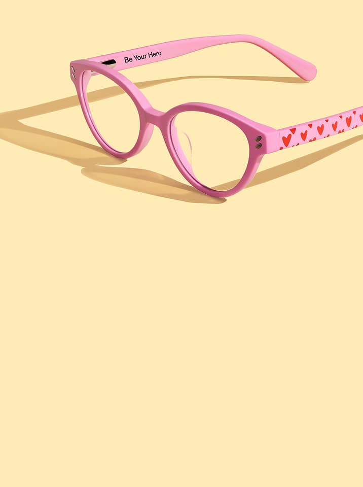 Wide angled photo of pink Zenni glasses with love heart patterned arms, on a pastel yellow background.