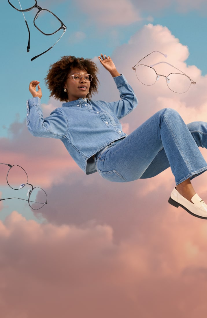A woman with curly brown hair wearing lightweight geometric glasses, floating in a semi-reclined position in front of a background of pink clouds and blue sky. More pairs of lightweight glasses are floating around her.