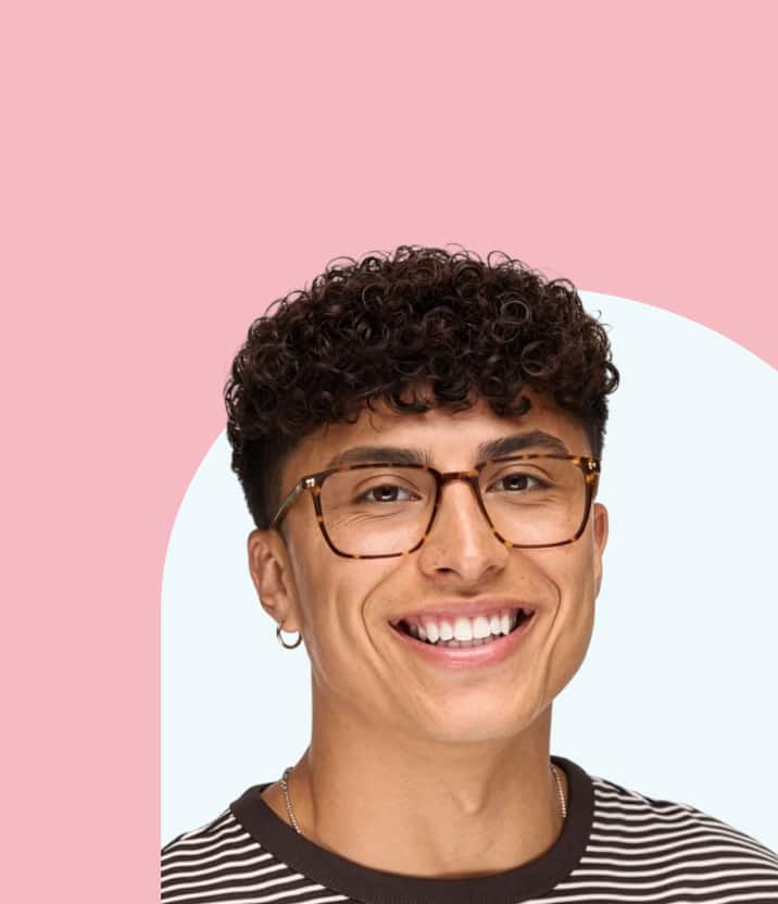 A smiling man with curly dark hair and a small hoop earring wearing classic tortoiseshell rectangular glasses, set against a pale blue and pink cloud-shaped background.
