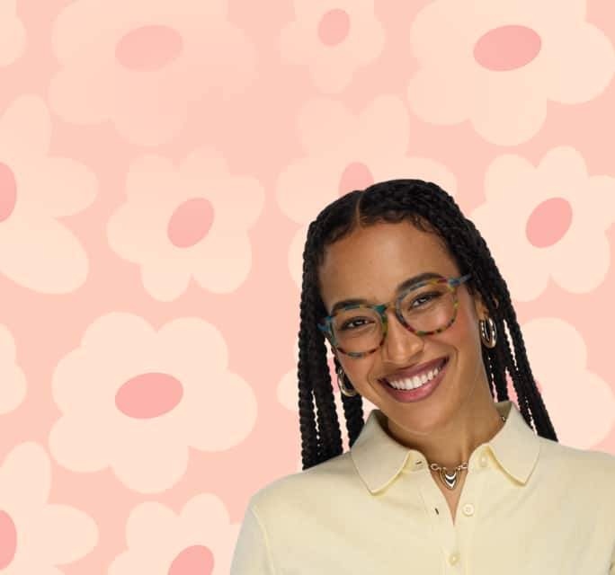 A smiling woman with long dark braids wearing round, multi-colored tortoiseshell glasses against a soft pink background with large flower illustrations.