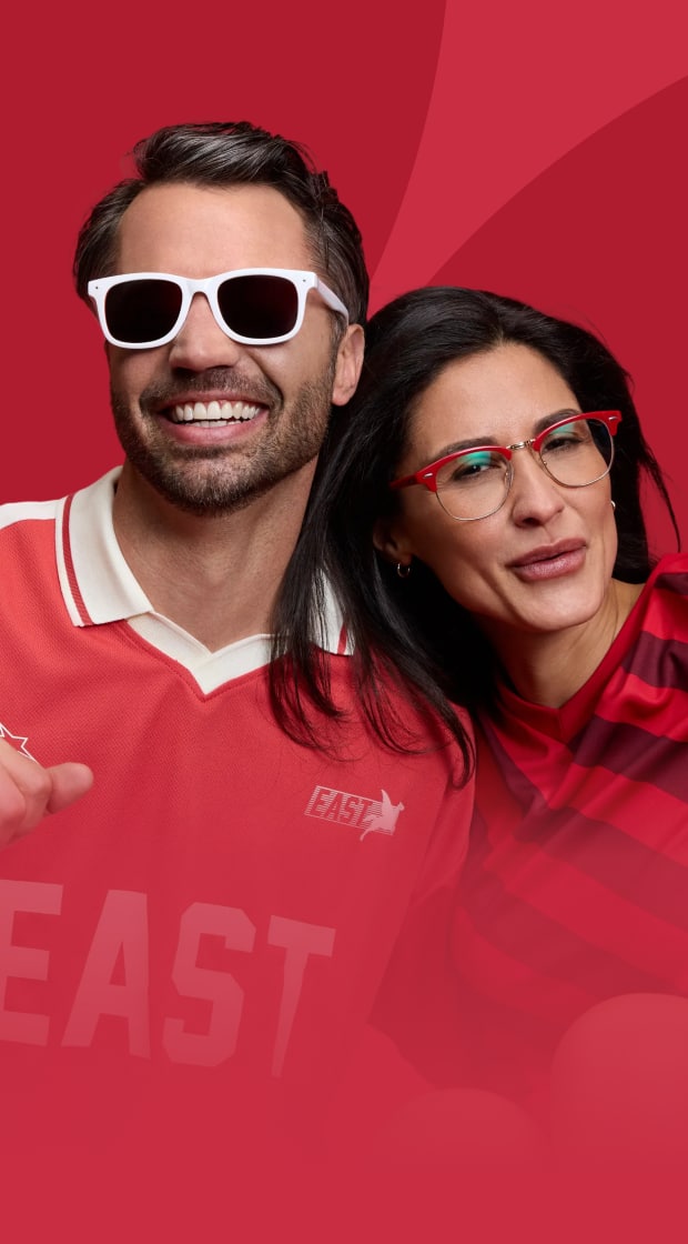 Smiling woman with red browline glasses and a smiling man with white sunglasses, both wearing red sports jerseys against a vibrant red background.