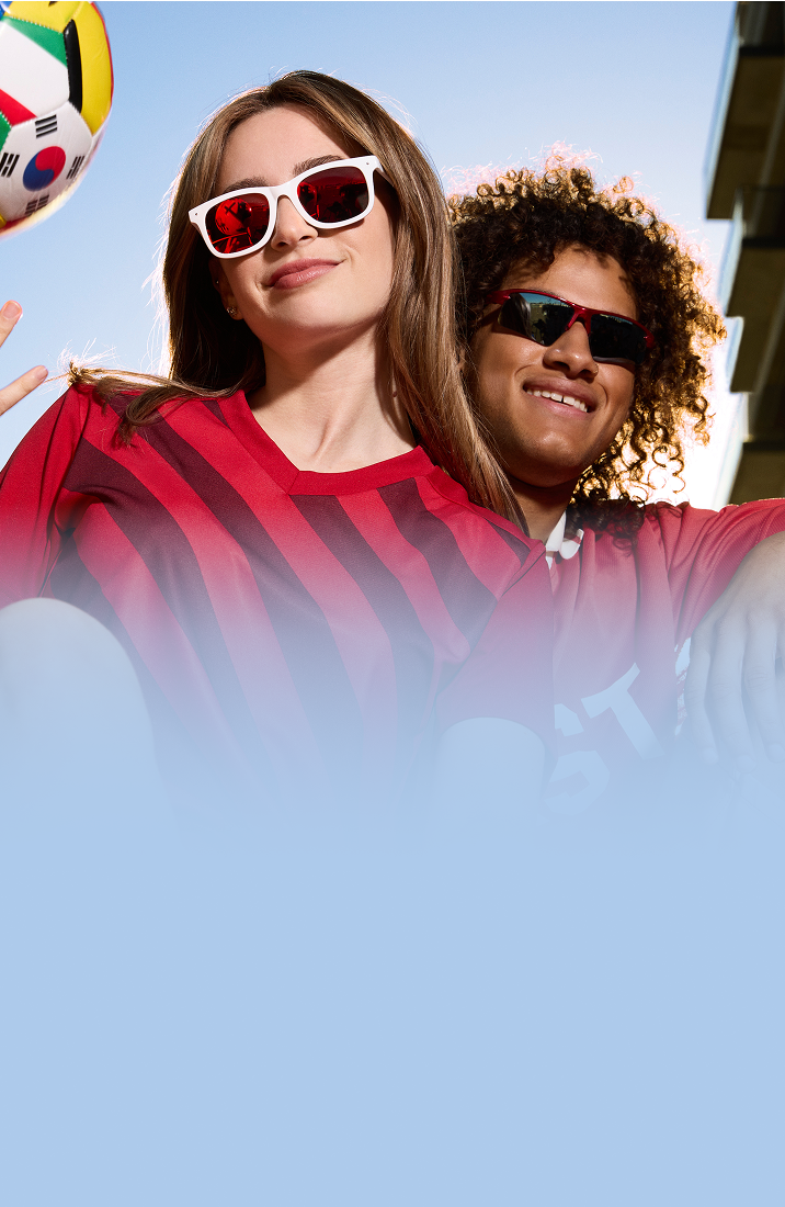 Two soccer fans wearing Zenni sunglasses, smiling with a soccer ball against a blue sky.