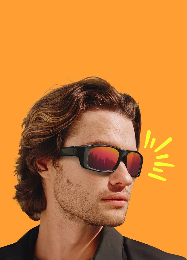Chase Stokes in mirrored Zunnies sunglasses, looking to the side against a vibrant orange background.