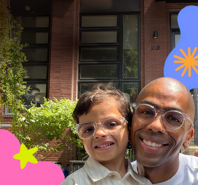 Darren and Ducky smiling together outdoors in matching clear eyeglasses against a brick building background with colorful star graphics.