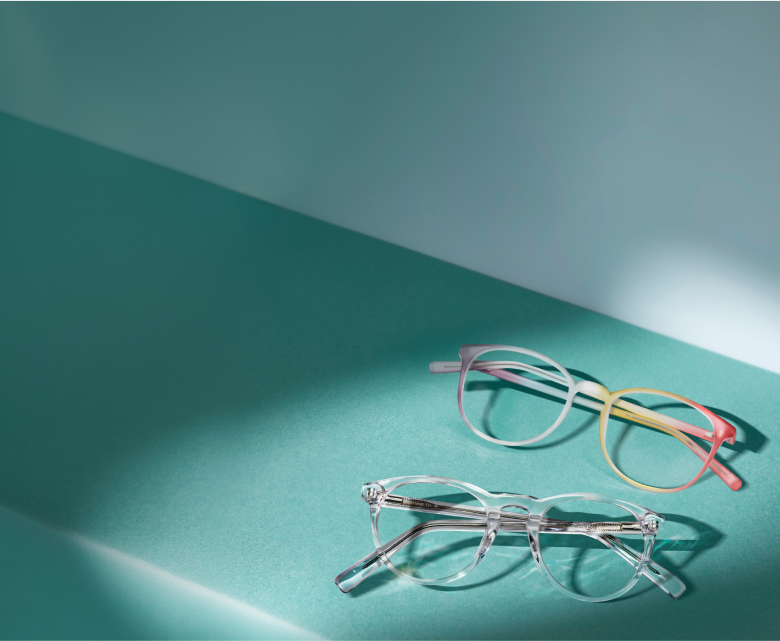 Two pairs of plastic glasses, one clear frames and one rainbow frames, on a teal shelf.