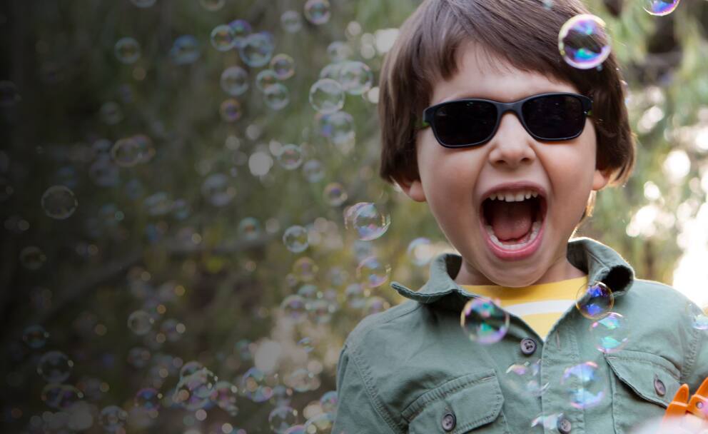 A kid wearing Zenni black rectangle sunglasses having fun surrounded by soap bubbles.