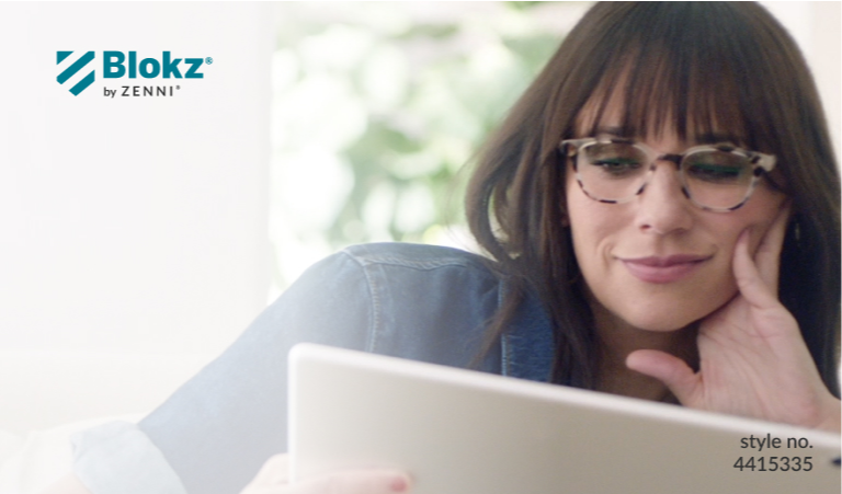 Image of Rashida Jones wearing Zenni glasses, sitting on her couch while reading her digital tablet.
