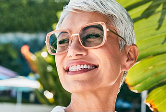 Image of a woman wearing Zenni glasses with blokz photochromic lenses in them, standing outside in the sun.