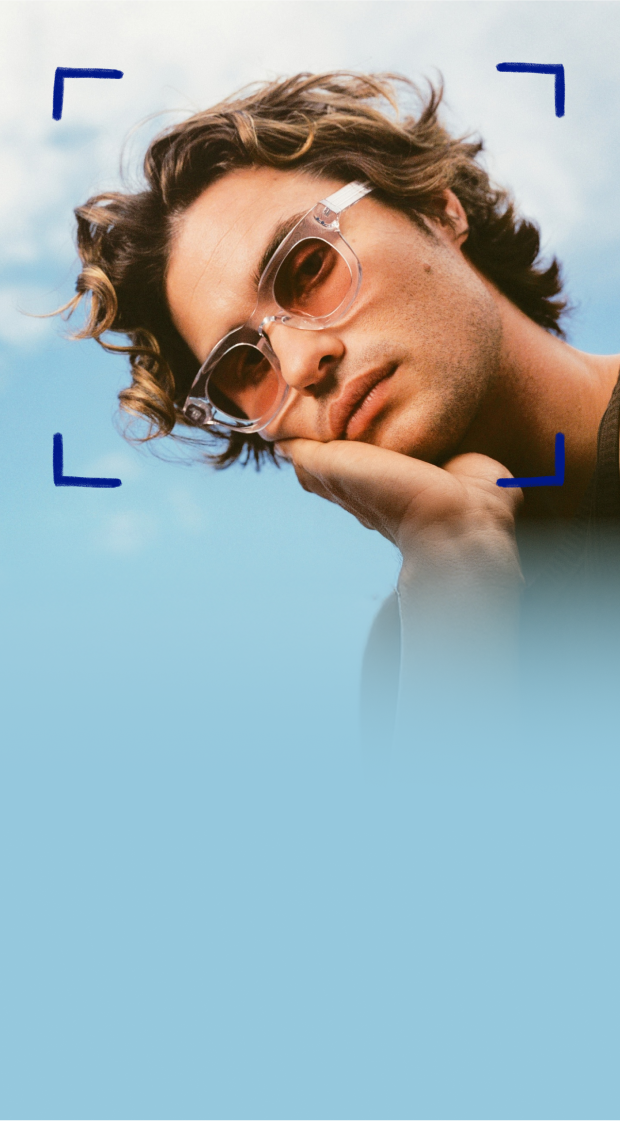 Chase Stokes wears Zenni frames with EyeQLenz featuring Zenni ID Guard lenses, posing outdoors under a bright sky.
