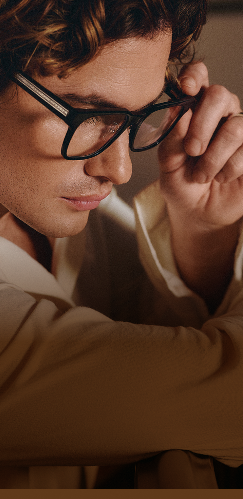 Chase Stokes puts on sleek black Zenni glasses while in a softly lit room.
