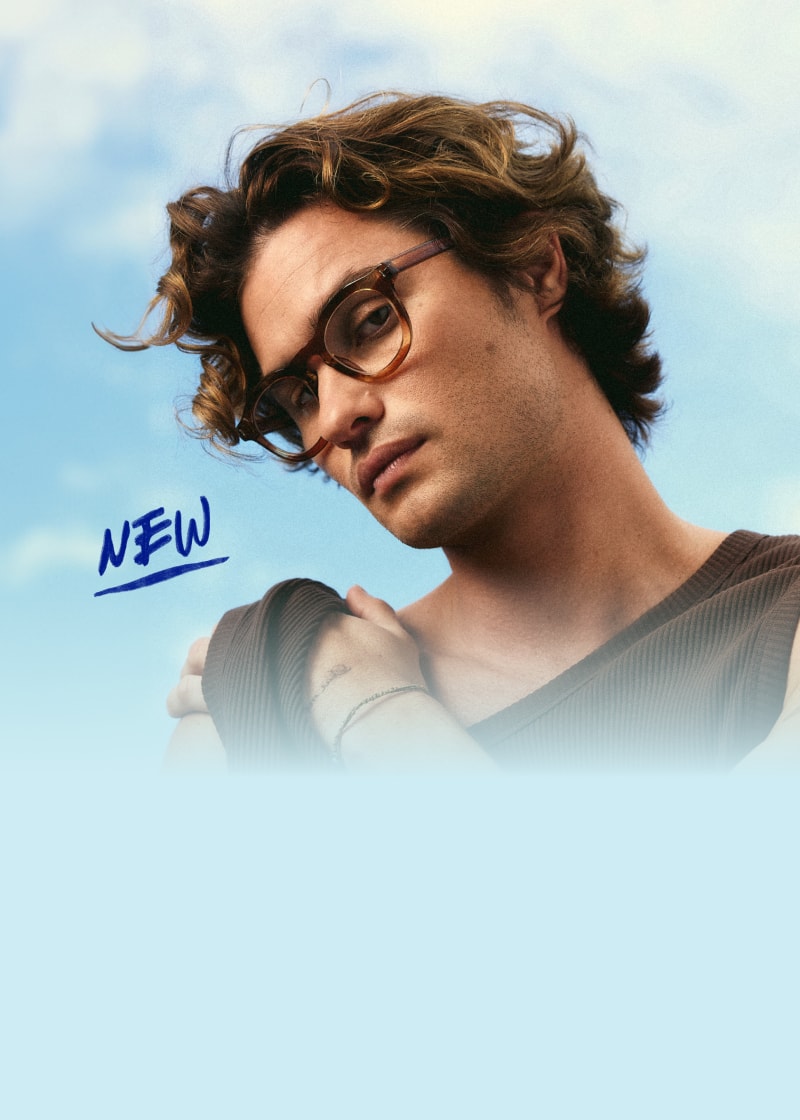 Chase Stokes wears oversized brown Zenni eyeglasses against a blue, clouded sky with a hand-written “NEW” in the foreground.