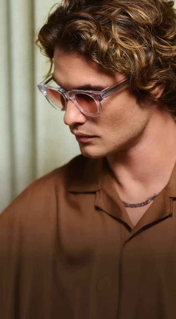Translucent round Zenni glasses with tinted lenses worn by Chase Stokes in front of a green curtain.