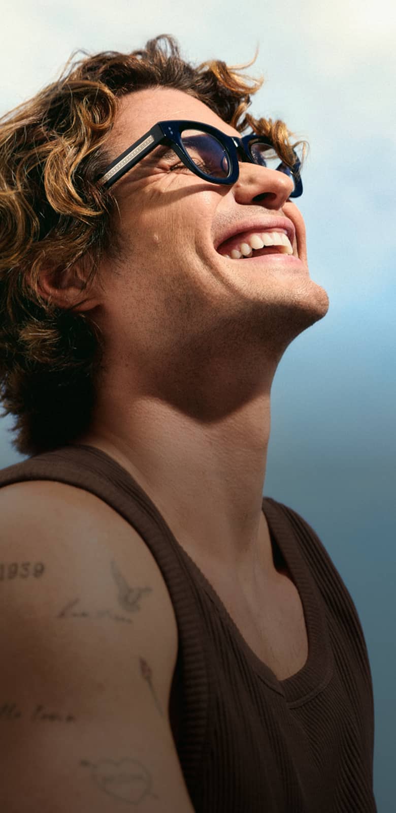 Black square Zenni sunglasses worn by a smiling Chase Stokes looking up at the sky.