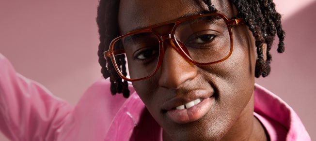 Man in pink jacket looking up while wearing Zenni oversized brown square glasses, pink background.
