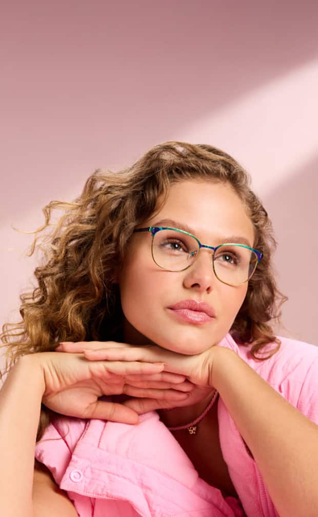 Woman in pastel pink jacket resting her chin on her hands, wearing Zenni teal glasses.