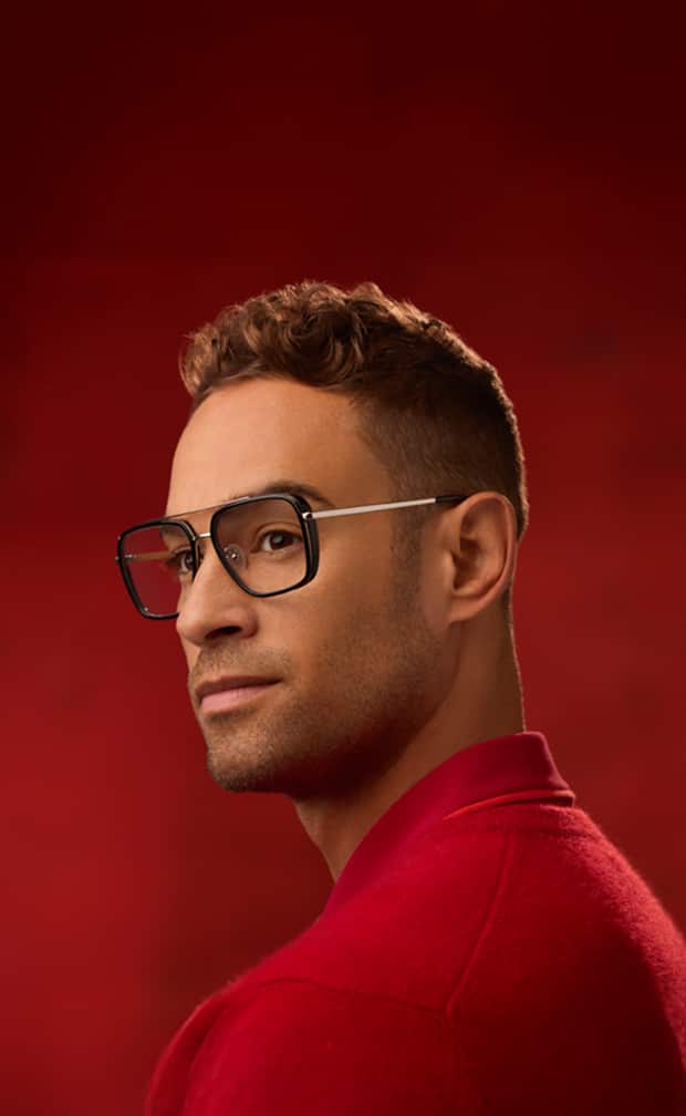 Male model in oversized square aviator-style Zenni glasses with black rims and gold metal accents, set against a red backdrop.