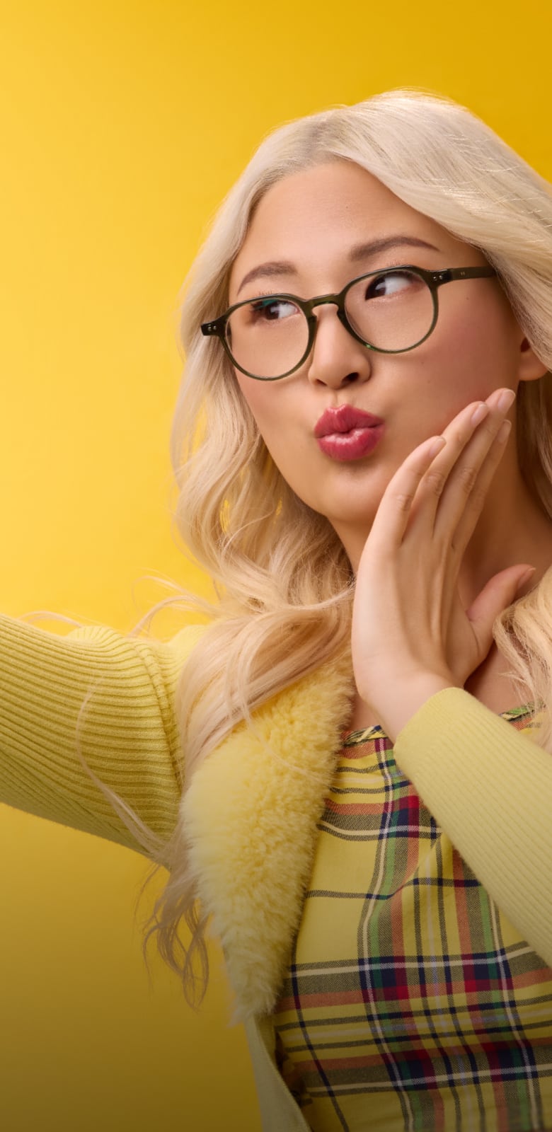 Blonde woman in playful round Zenni glasses snapping a selfie against a vibrant yellow background