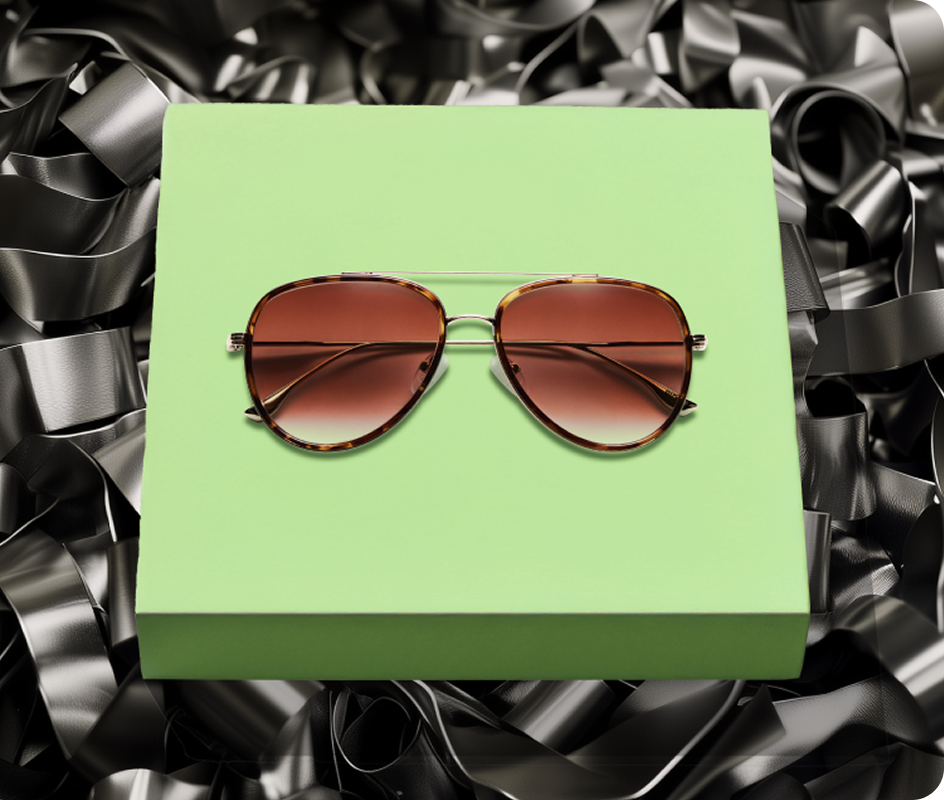 Brown EcoBloomz aviator sunglasses displayed on a light green platform surrounded by recycled rubber, representing the eco-friendly eyewear collection.