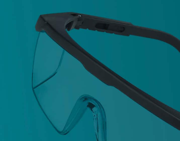 Protective goggles with black frames on a teal background.