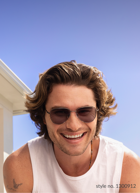 Chase Stokes smiling outdoors in a white tank top, sporting Zenni EyeQLenz glasses with a dark tint.