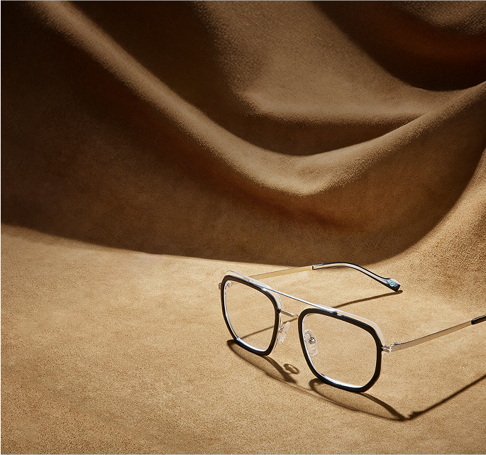 Square black and silver aviator glasses on a brown suede surface.