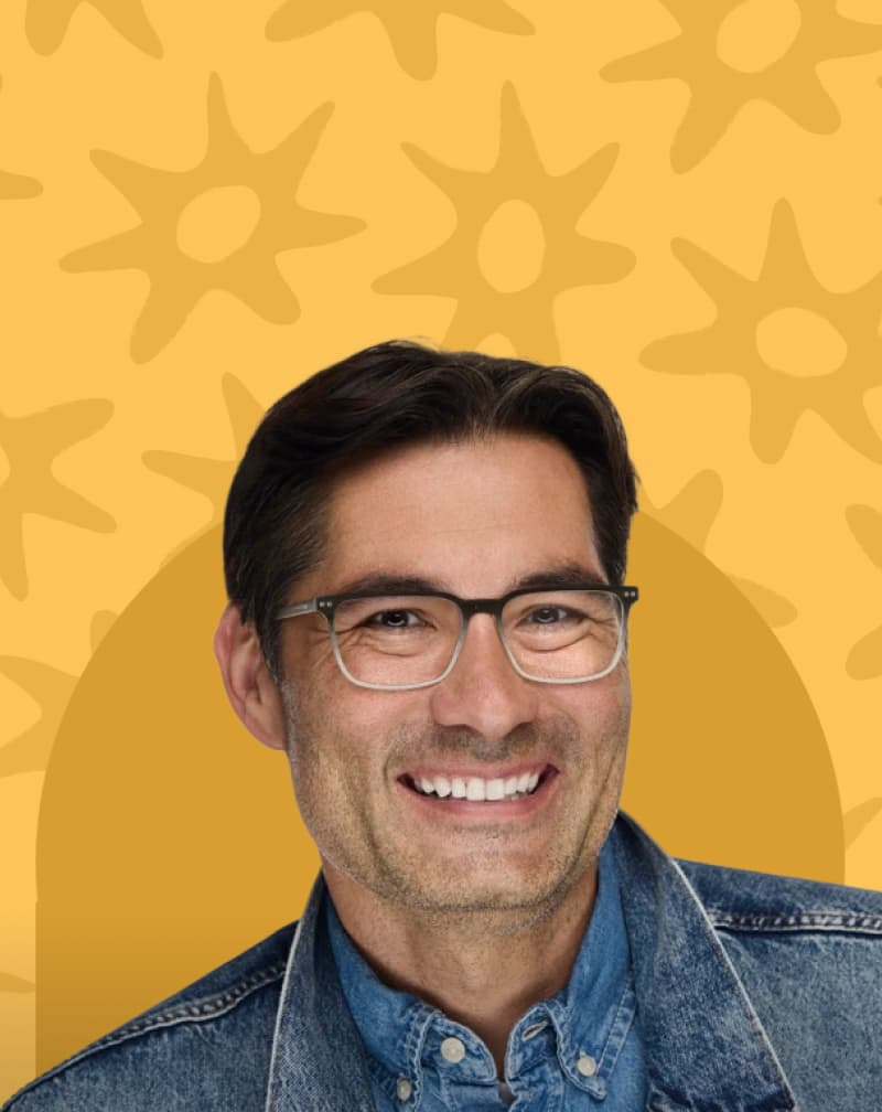 Smiling man wearing gradient rectangular eyeglasses against a warm yellow background with starburst pattern illustrations.