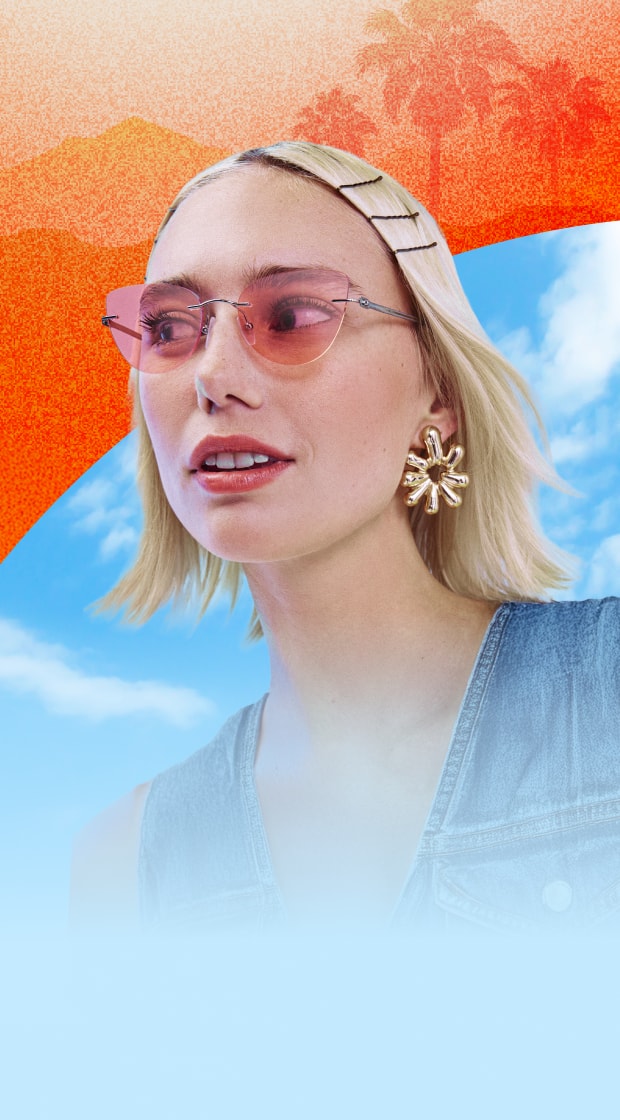 A woman with short blond hair and statement earrings, wearing cat-eye rimless Zenni sunglasses with pink lenses. Blue sky and hazy orange desert background.