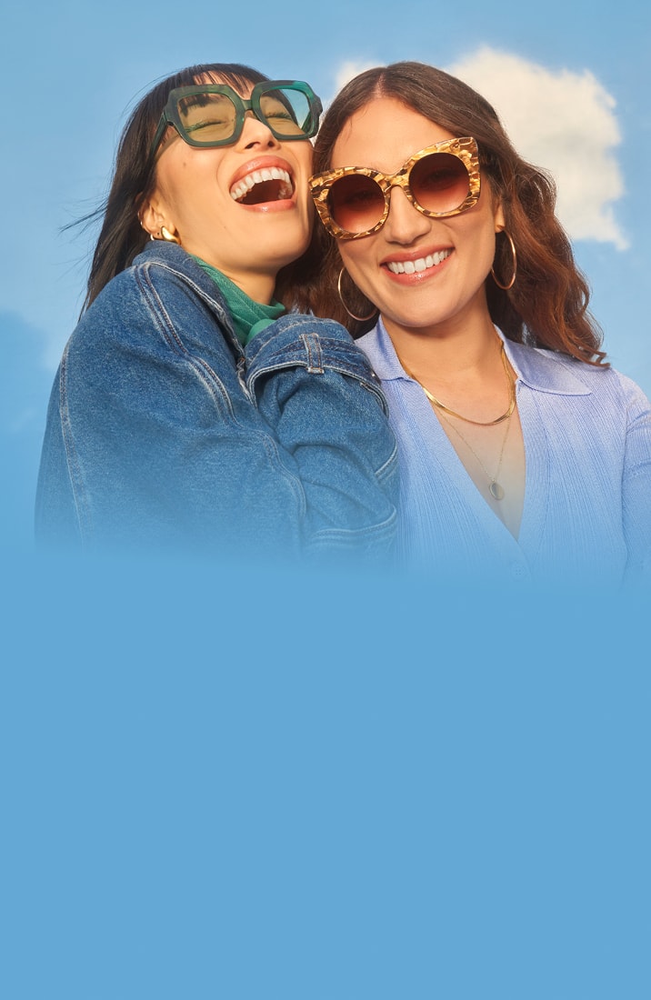Two women smiling and wearing stylish sunglasses, embracing against a bright blue sky with clouds, alongside large text promoting savings on glasses with vision insurance, FSA, and HSA.