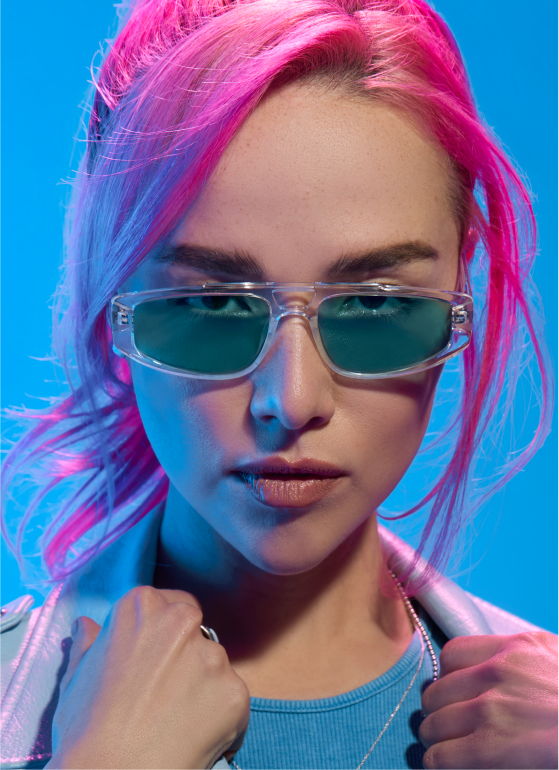 A woman with pink hair wearing plastic aviator glasses with blue lenses.