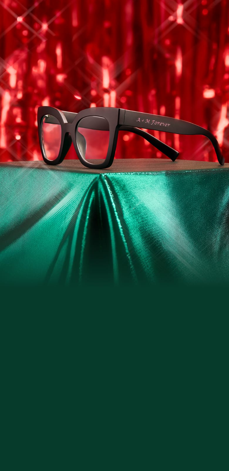 Black Zenni eyeglasses with "B & K Forever" custom engraving on temple arm against festive red and green holiday lights background.