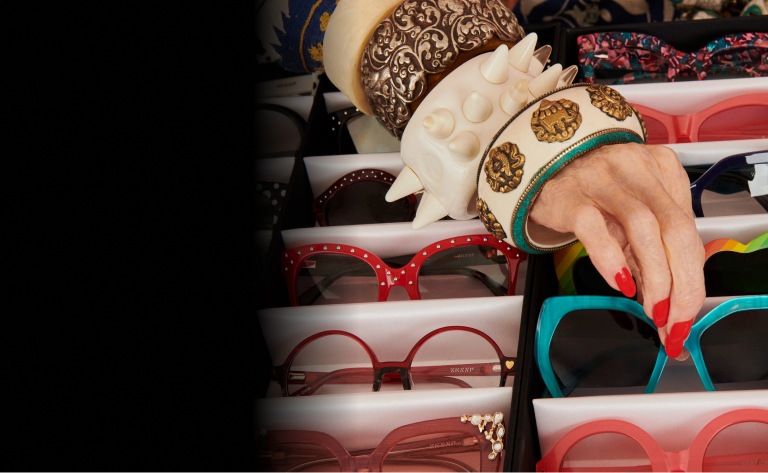 Image of a selection of the Iris Edit frames, with Iris’s hand picking out a pair of turquoise cat-eye sunglasses.