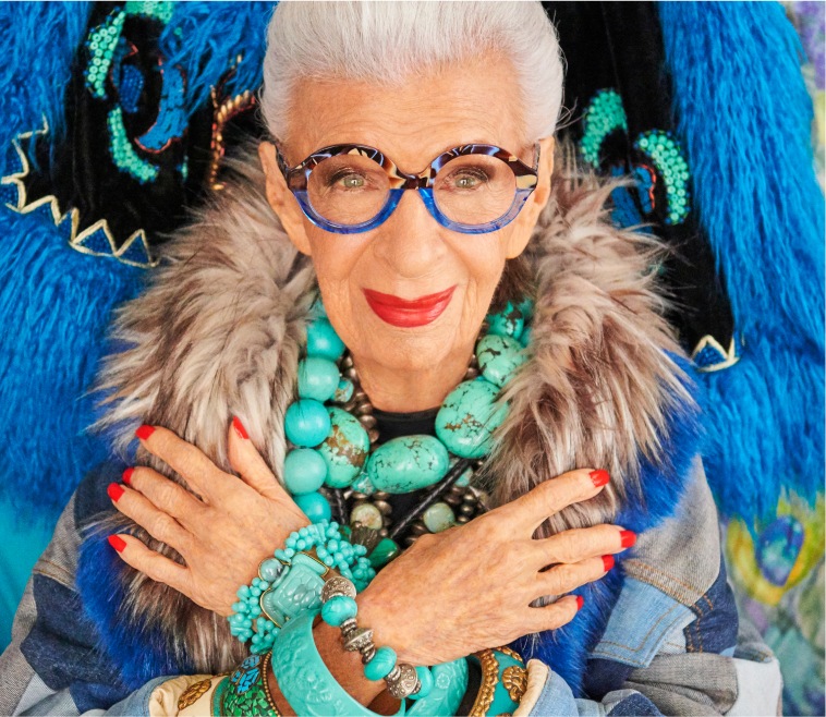 Image of Iris Apfel wearing Zenni half & half round glasses #4453239. She is crossing her arms and is standing in front of bright blue artwork on a wall.