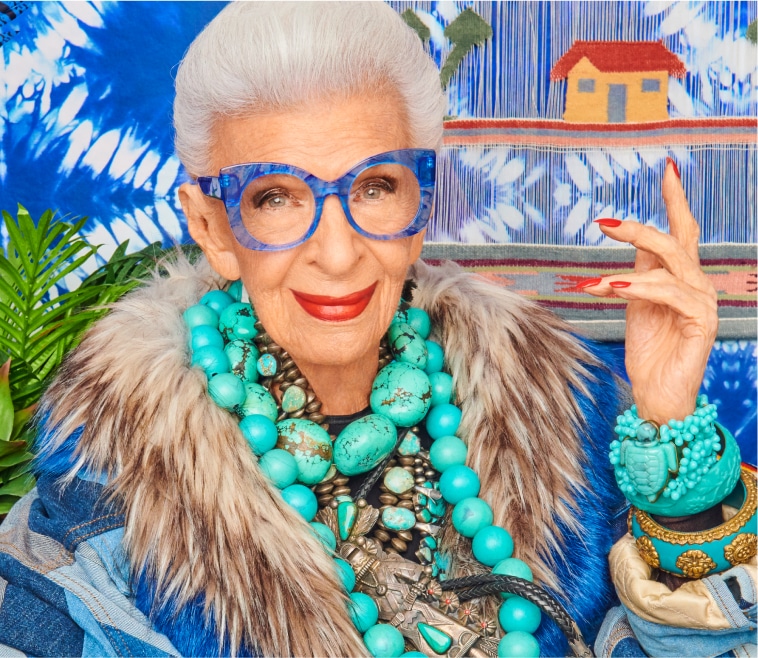 Image of Iris Apfel wearing Zenni What’s New Pussycat cat-eye glasses #4452616. She is wearing large turquoise jewelry and is standing in front of a tie dye-printed wall.
