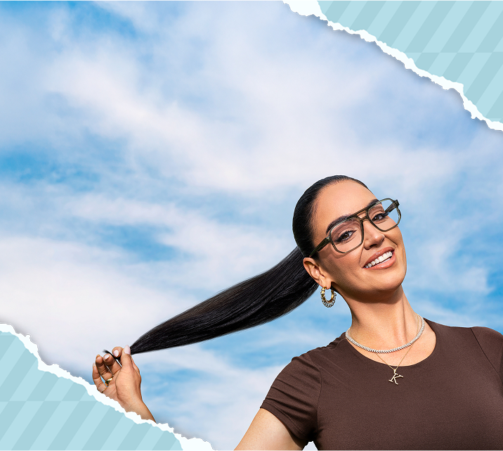 Claire Kittle with aviator glasses and a ponytail against a blue sky background, wearing a brown top and gold jewelry.
