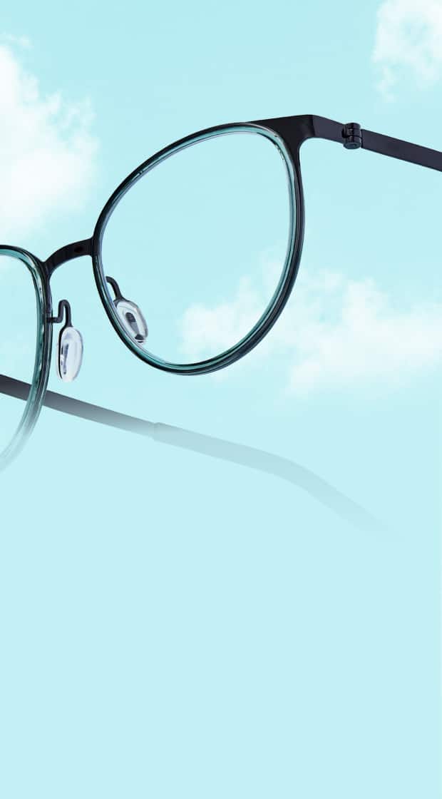 Lentes redondos ligeros con montura delgada de color verde oscuro flotando en ángulo contra un cielo azul brillante lleno de suaves nubes blancas.