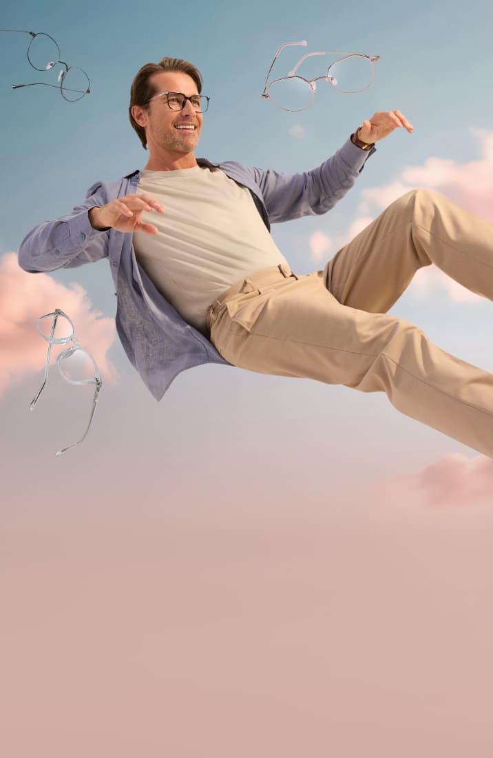 A man with brown hair wearing gray square glasses, floating in a semi-reclined position in front of a background of pink clouds and blue sky. More pairs of lightweight glasses are floating around him.