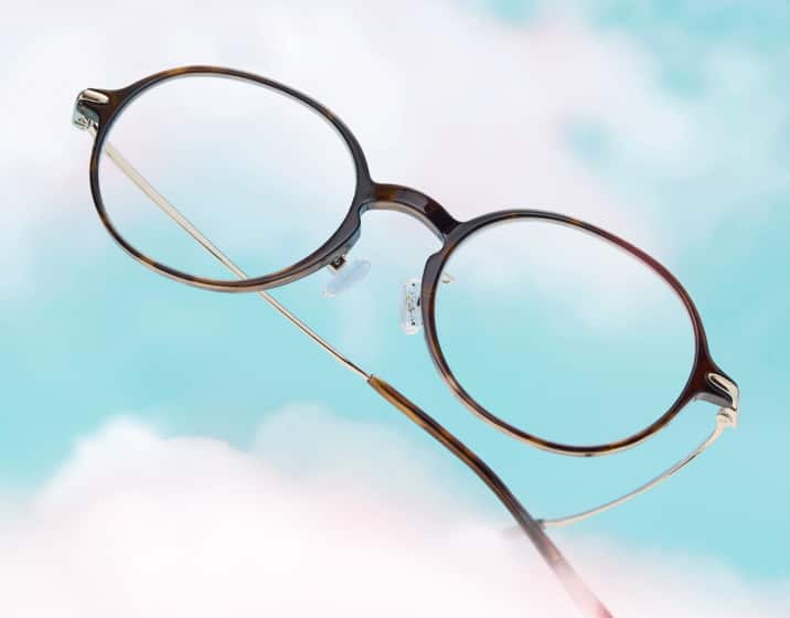 Round tortoiseshell glasses floating on a background of blue sky with fluffy clouds.
