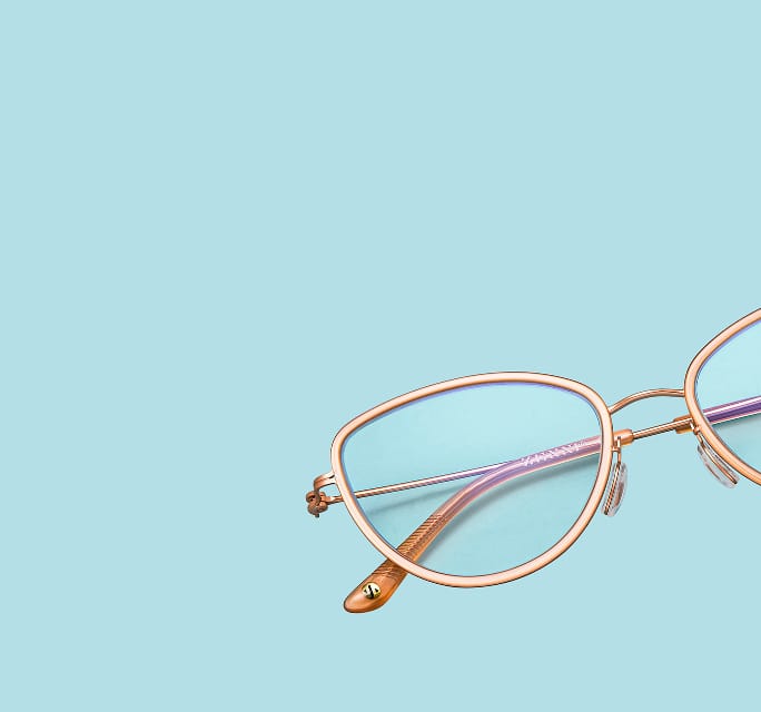 Close-up of rose gold cat-eye eyeglasses with thin metal rims and translucent pink temples, floating on a solid light blue background.