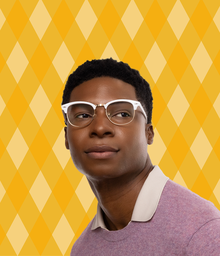 A man with short curly black hair wearing white browline glasses, on a yellow background with a diamond lattice motif.